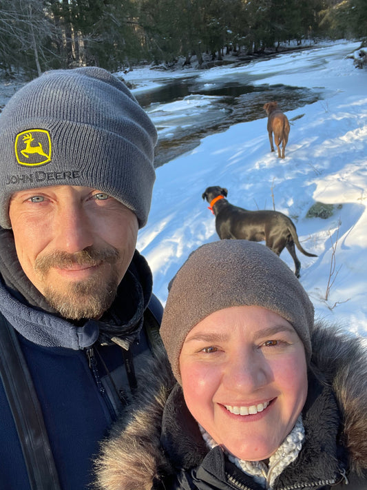 Nick and Brandy standing together on their forest property at Florence Farmstead, smiling and surrounded by nature